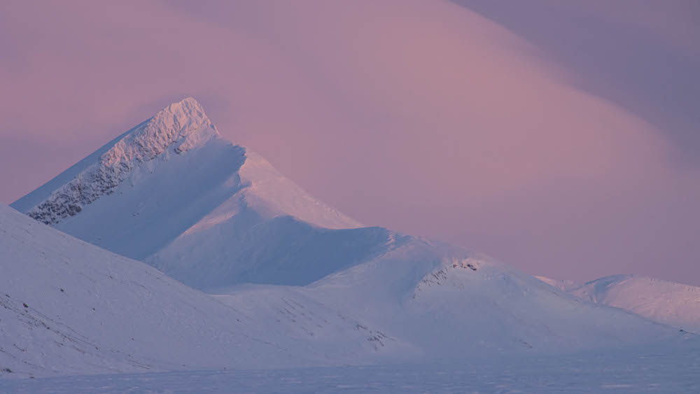 Verschneiter Berggipfel vor rotem Himmel