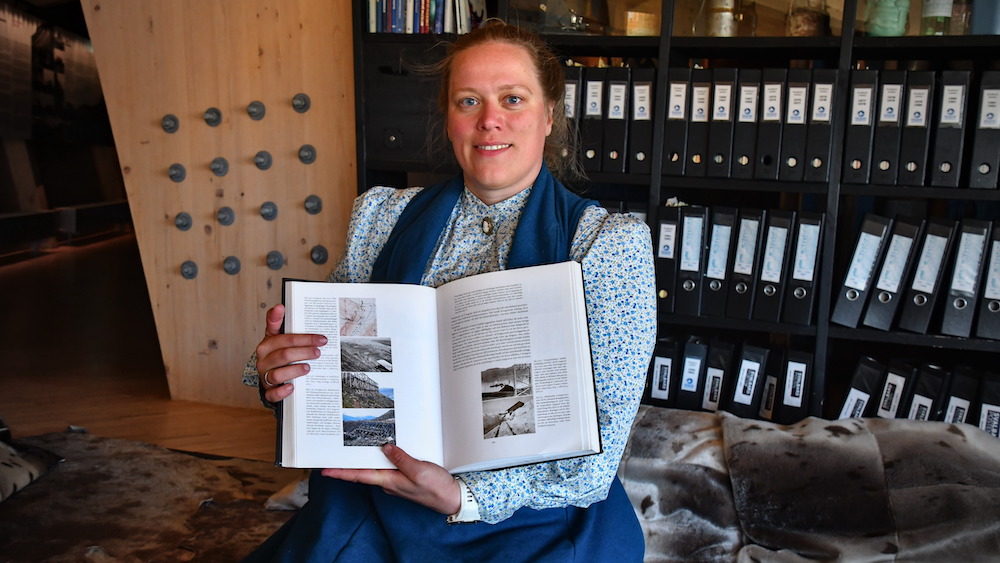 Guide Katharina sits in historical clothing on sealskins and holds a book.
