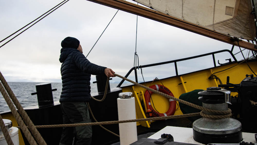 A person pulls on a rope while sailing with the SV Meander