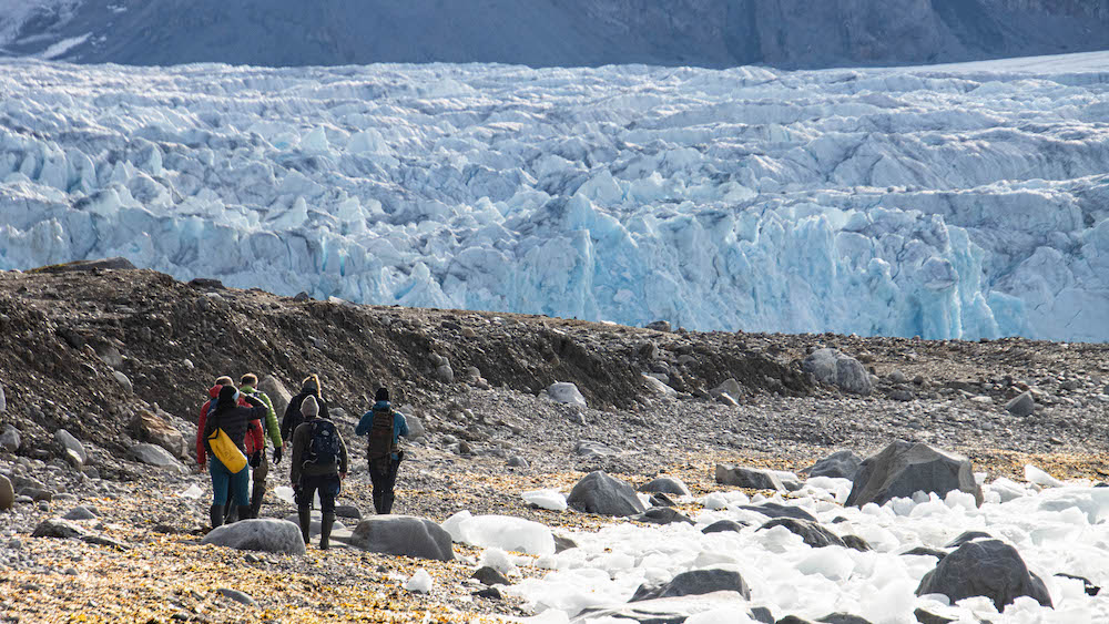 Several people on a beach with glacial ice in front of a glacier front