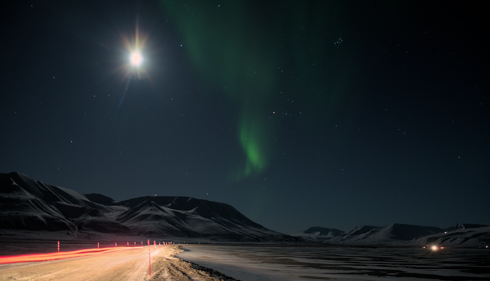 Grüne Nordlichter im Adventdalen, während ein Auto auf der Straße fährt