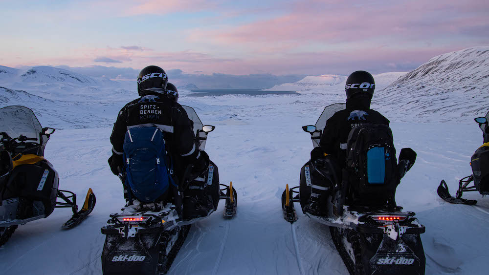 A group of guests on snowscooters against a red sky