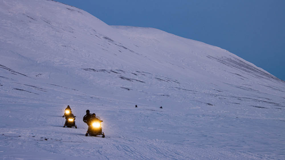 Three snowmobiles driving with their lights on